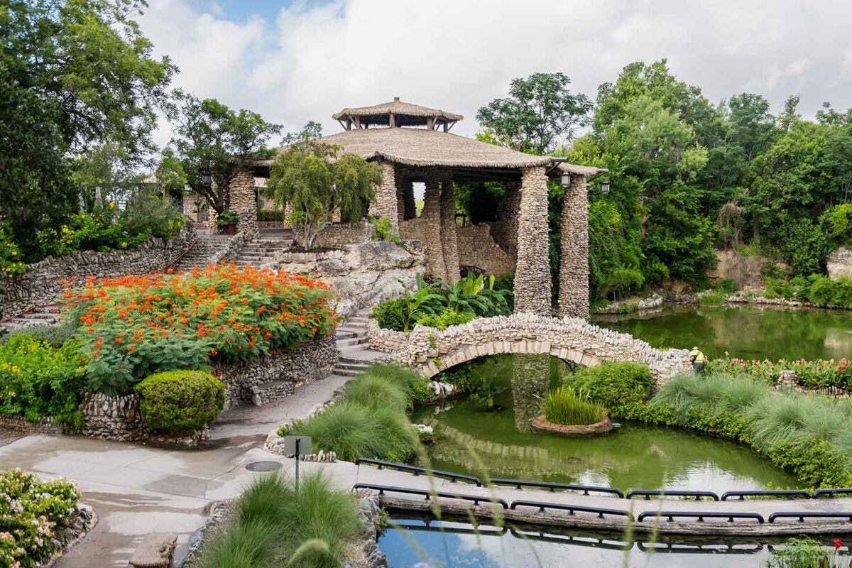 Japanese tea garden with bridge and pavilion pictured and plants.